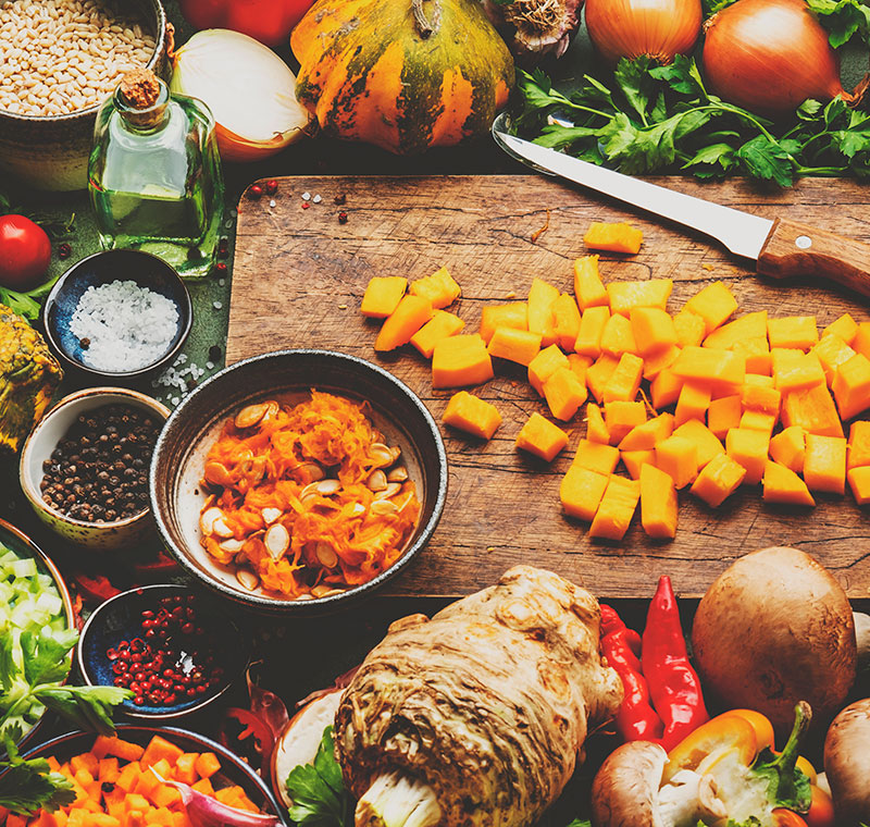 Food background. Diced raw peeled pumpkin and vegetable knife on rustic wooden cutting board. Vegetables, mushrooms, roots, spices - ingredients for vegan cooking. Healthy eating, diet, comfort slow food concept. Top view